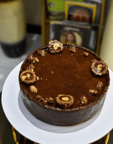 Homemade chocolate cheesecake in Lahore topped with Ferrero Rocher on white cake stand by Exoticake bakery.