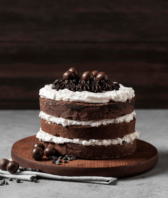 Homemade chocolate layer cake in Lahore with cream frosting layers and chocolate topping on wooden stand